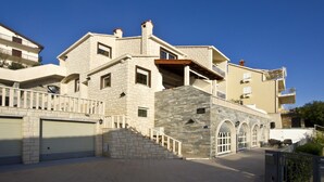 A multi-story residential building with a stone facade, multiple balconies, and a central staircase leading to the entrance.