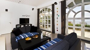A modern living room with a sofa, a coffee table with snacks, a TV, and a large window with a view.