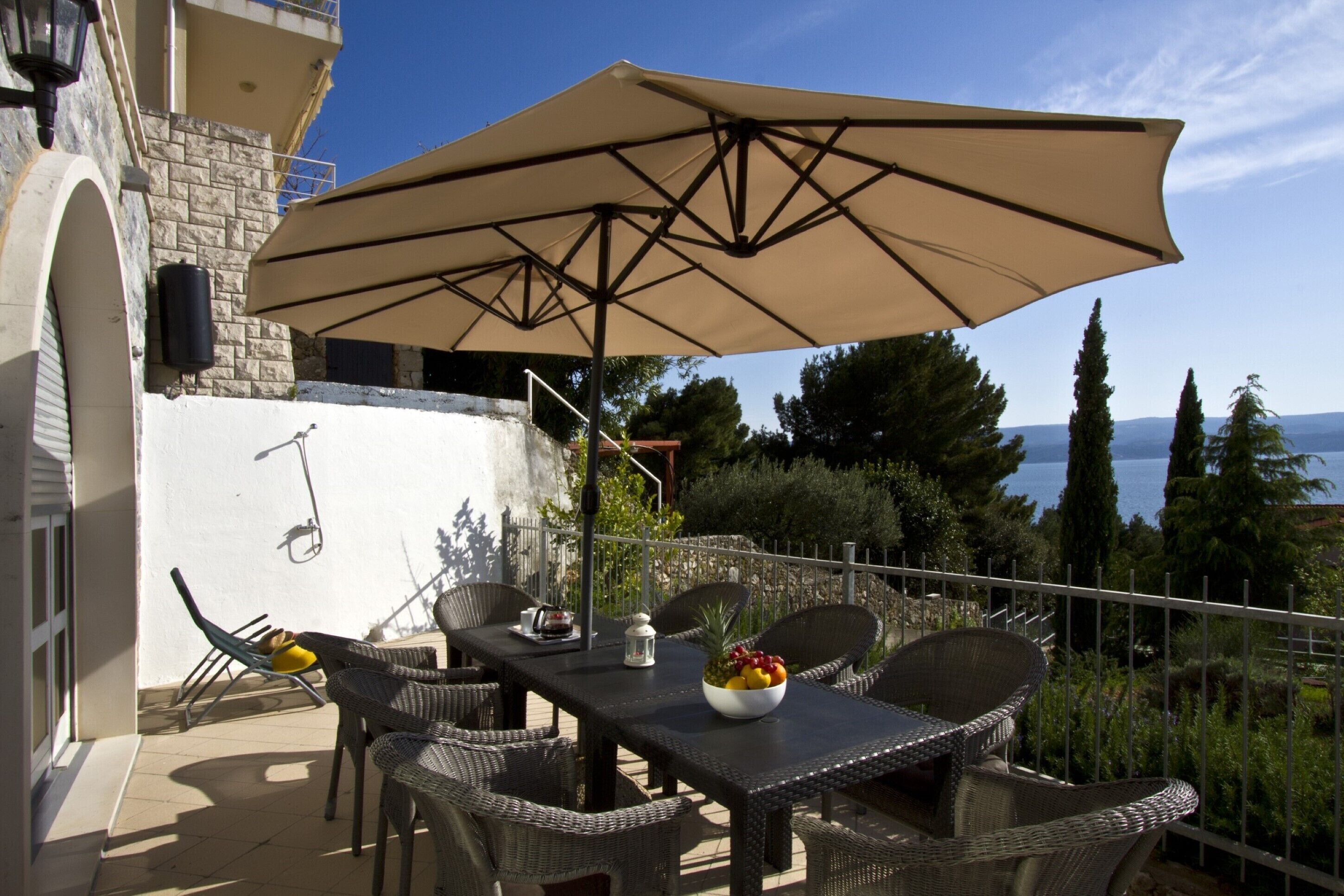 An outdoor patio with wicker furniture, a table with a bowl of fruit, and a large umbrella.