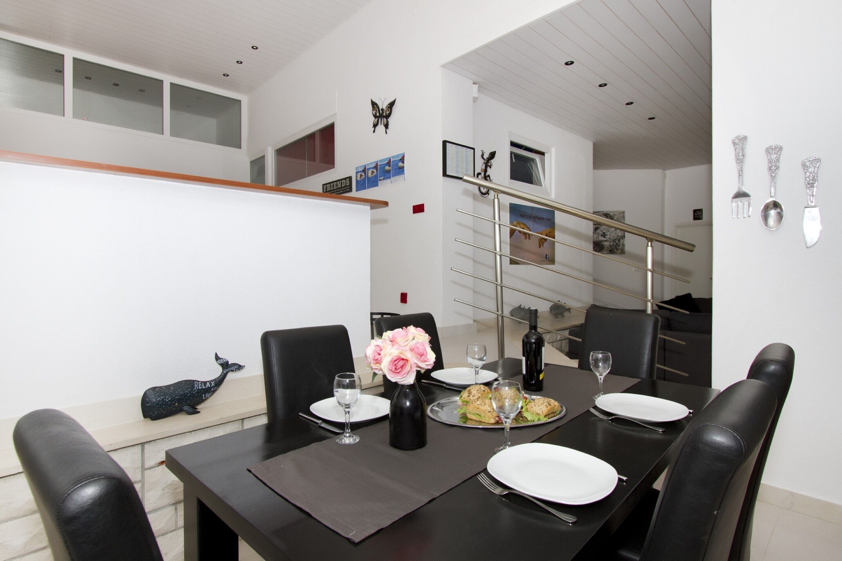 A dining area with a black table set for four, a vase of pink flowers, and a whale decoration on the wall.