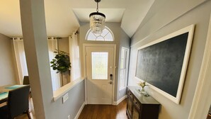 Um corredor com piso de madeira, um candelabro, uma porta com vitral e um quadro negro grande na parede.