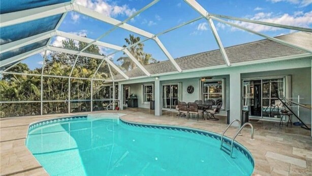 Piscina coberta com área de terraço, terraço coberto com mesa e cadeiras, e um edifício com fachada azul clara.
