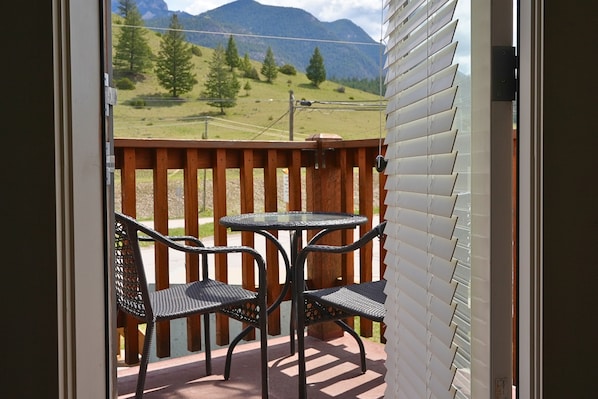 A balcony with a table and chairs, offering a view of a mountainous landscape. - Modern and Bright 2BDR/2BR Condo with Mountain Views (Radium Hot Springs)