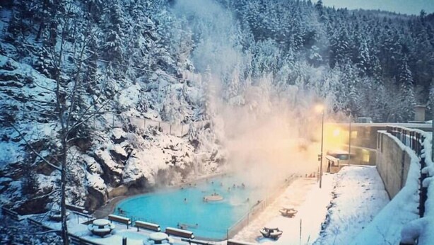 Ein mit Schnee bedeckter Außenpoolbereich mit Bänken und einem Whirlpool, umgeben von Bäumen.