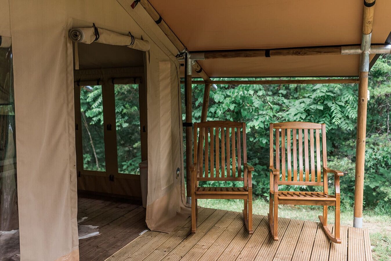 Une terrasse en bois avec deux fauteuils à bascule placés sous une tonnelle, le tout entouré de verdure.