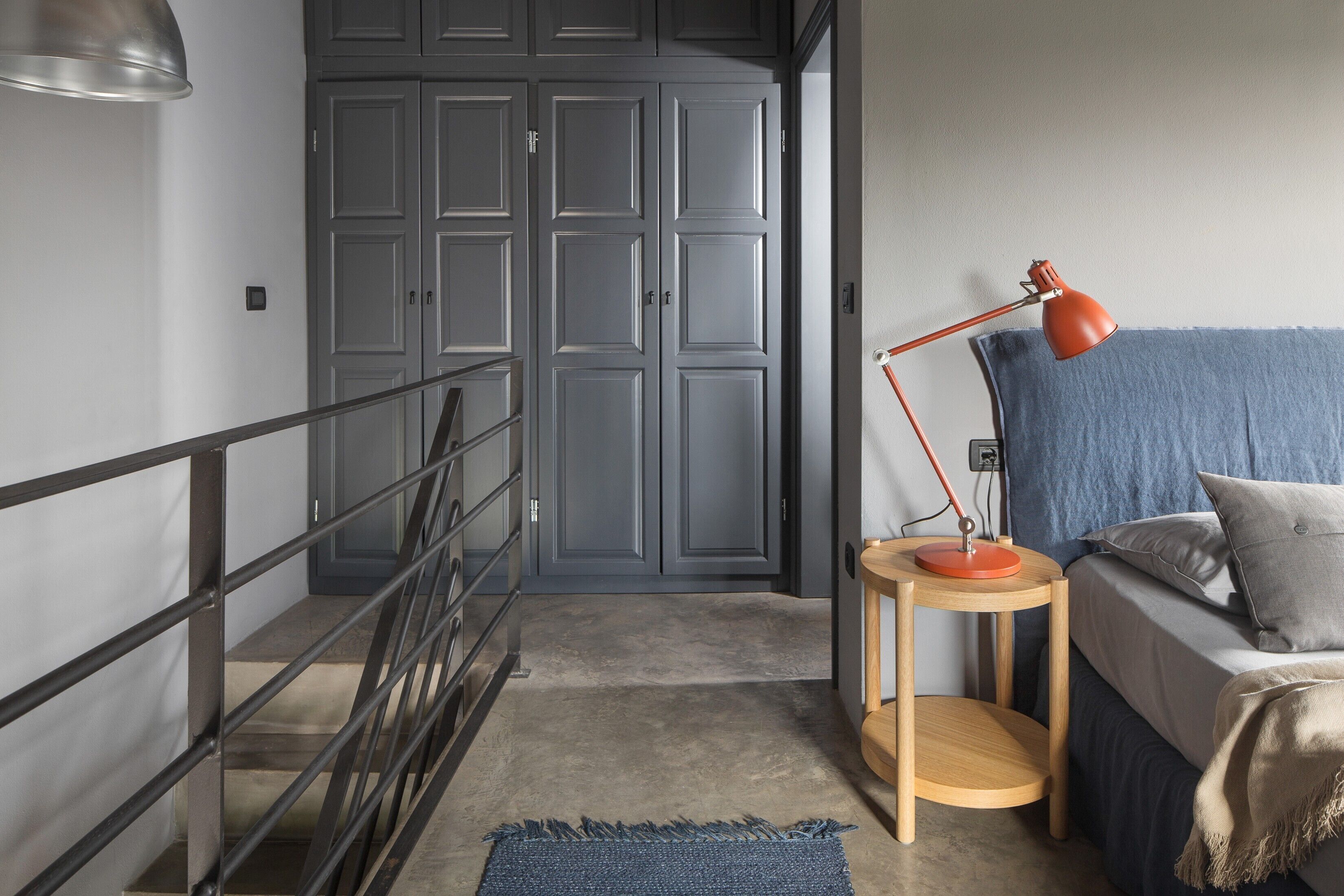 A bedroom with a bed, a nightstand, a lamp, a blue curtain, and a grey wardrobe.