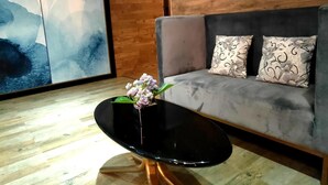 Una sala de estar moderna con un sofá gris, cojines estampados, una mesa de centro negra con un jarrón de flores y arte abstracto en la pared.