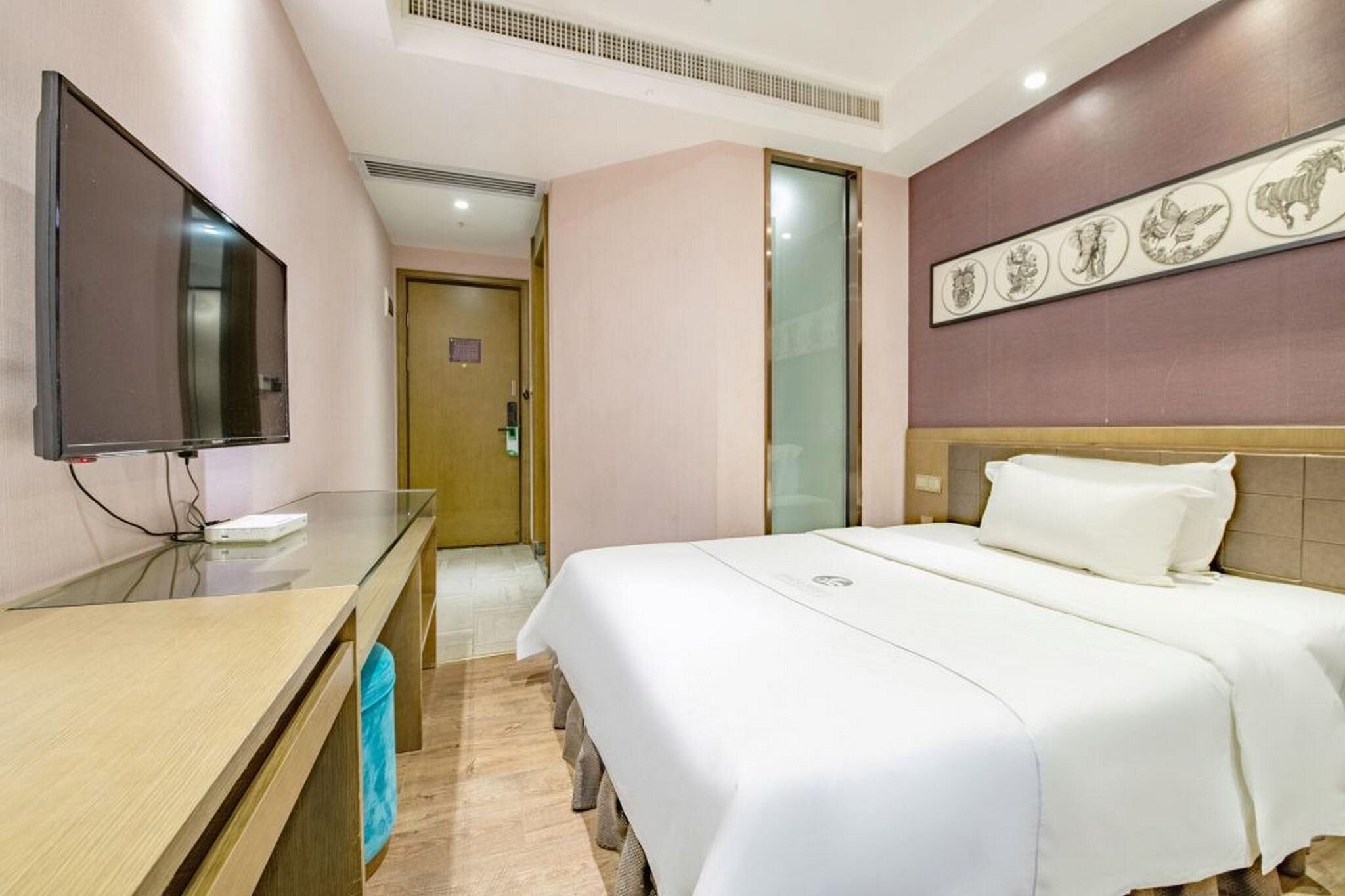 A hotel room with a bed, a TV on a desk, and a door leading to another room.