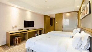 Habitación de hotel con dos camas, un escritorio, un televisor y un espejo grande.