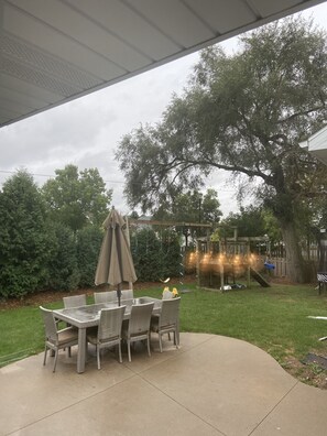 Une terrasse extérieure avec une table et des chaises, entourée d’une pelouse verdoyante et d’arbres.