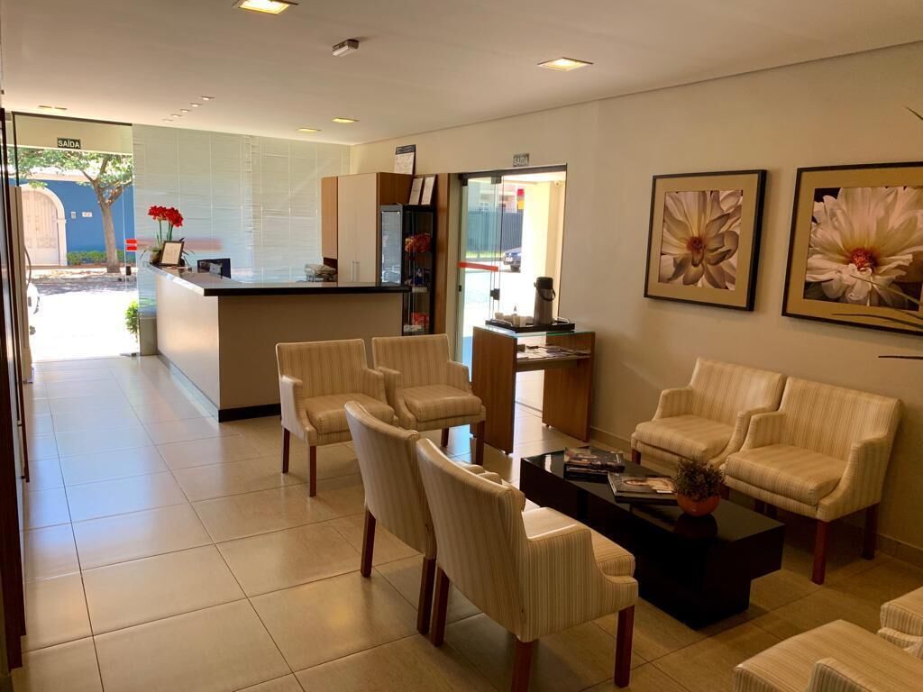 Um hall de hotel com balcão de recepção, área de estar e quadros com flores nas paredes.
