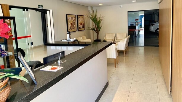 A reception area with a counter, chairs, a plant, and a sign indicating the exit. - Hotel Flat Alameda (Aracatuba)