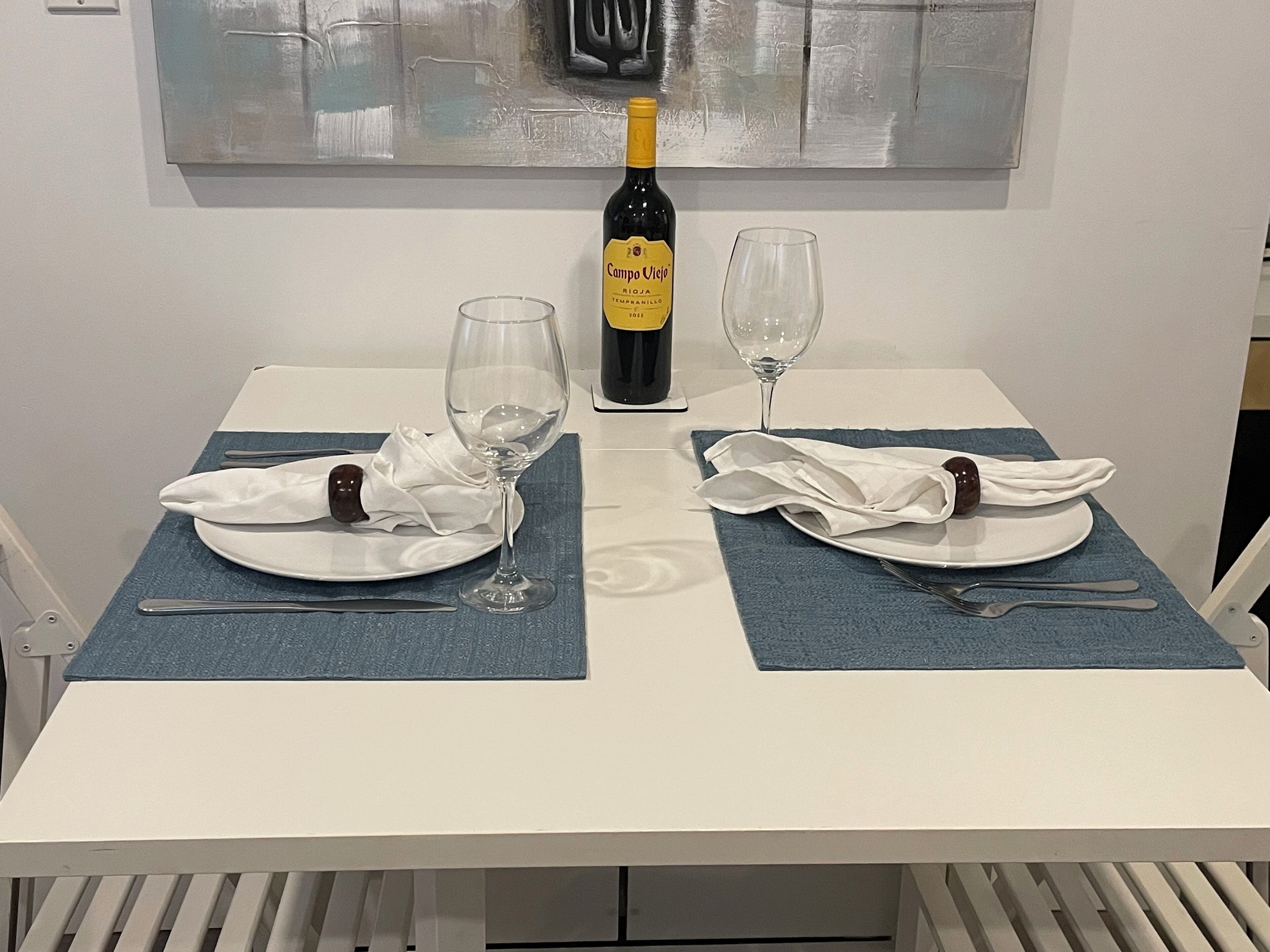 A dining table with two plates, cutlery, and wine glasses, set for two.