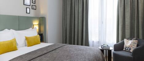 Una habitación de hotel con cama, una silla, una mesita y ventana con cortinas.