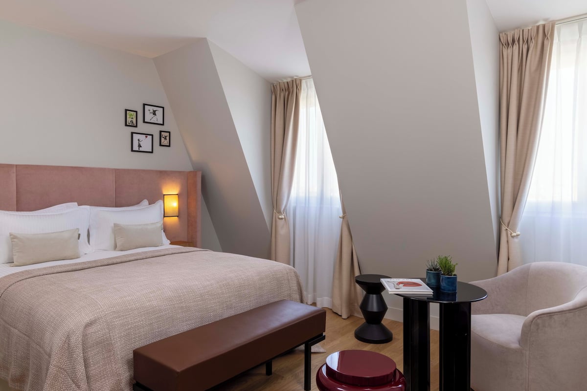 A modern hotel room with a large bed, a bench, a small table with a plant, and a chair.