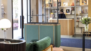 Un área de recepción con un sofá verde, un mostrador de madera y una pared con estantes que exhiben diversos objetos.