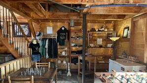 A rustic wooden interior with a dining table, chairs, a foosball table, and a clothing rack with various garments.