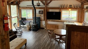 A rustic cabin interior with a stone fireplace, wooden dining table, and a television.