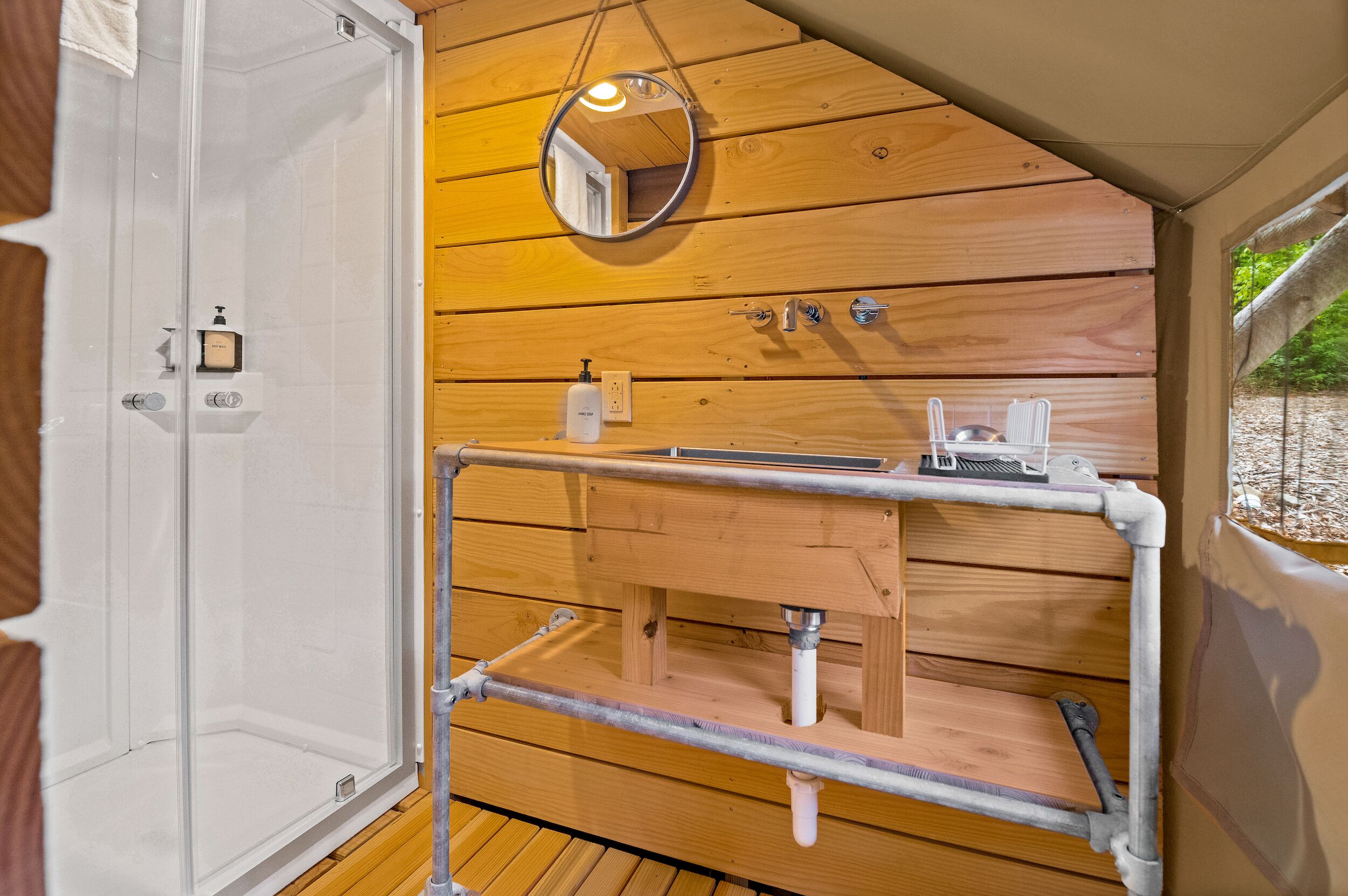 Une salle de bain rustique, aménagée dans une cabane en bois, avec une douche, un lavabo et un miroir.