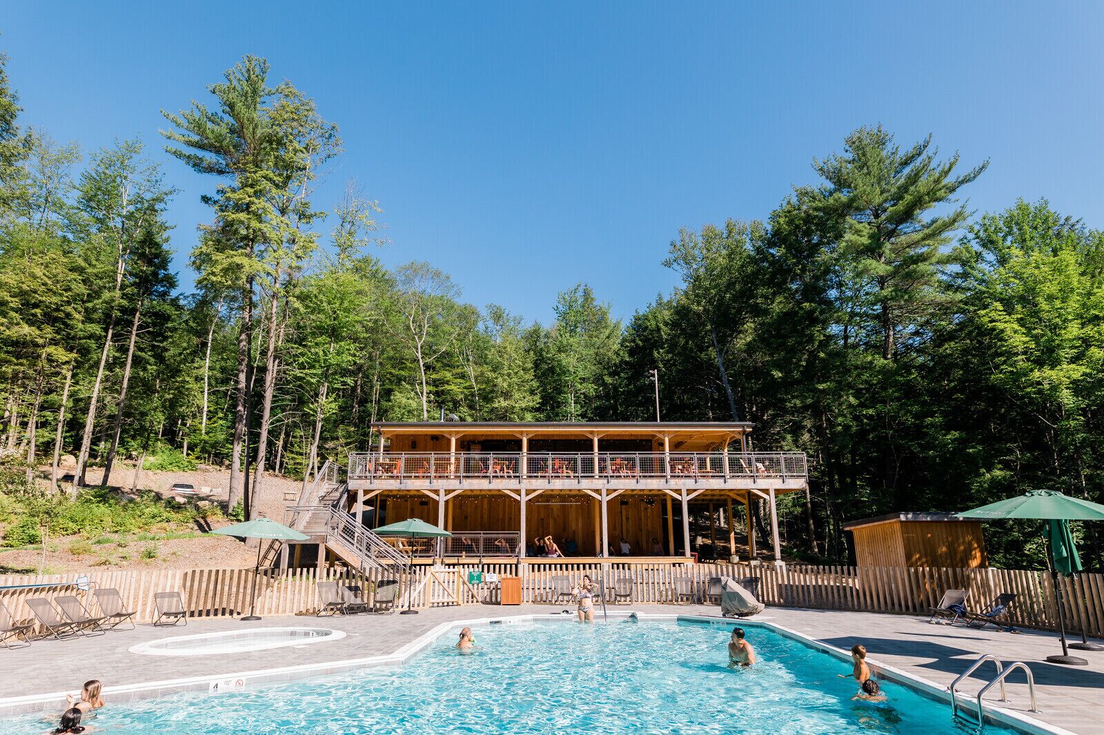 A wooden cabin with a pool, surrounded by trees.