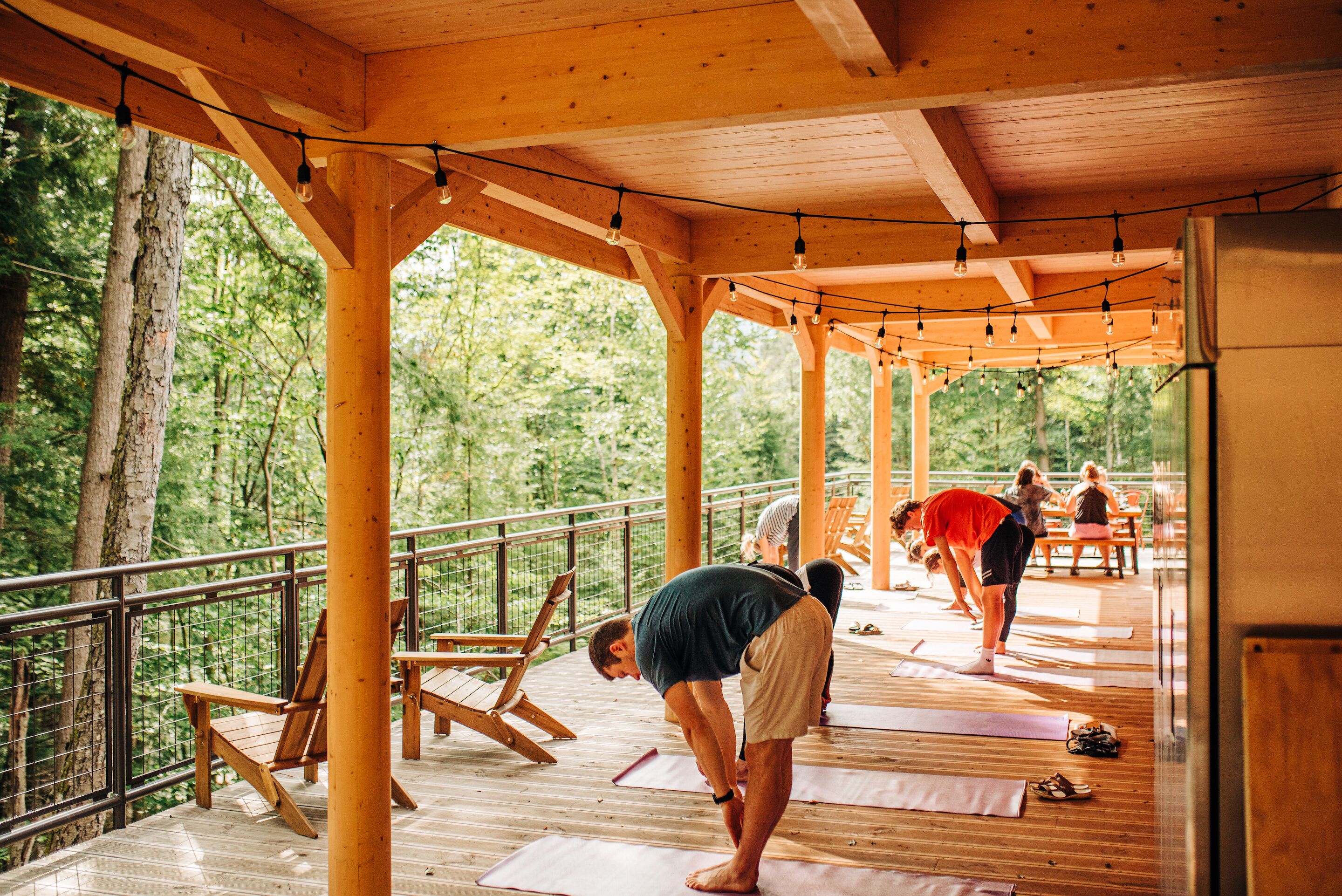 An outdoor wooden deck with yoga mats and chairs, surrounded by trees.