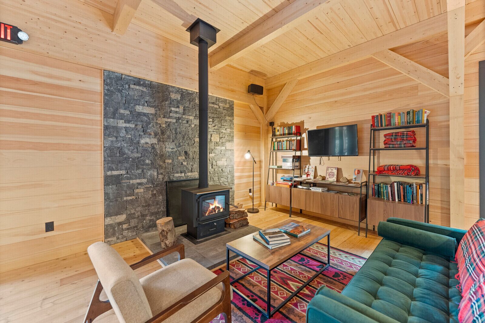 A cozy living room with a stone wall, a fireplace, wooden furniture, and a bookshelf.