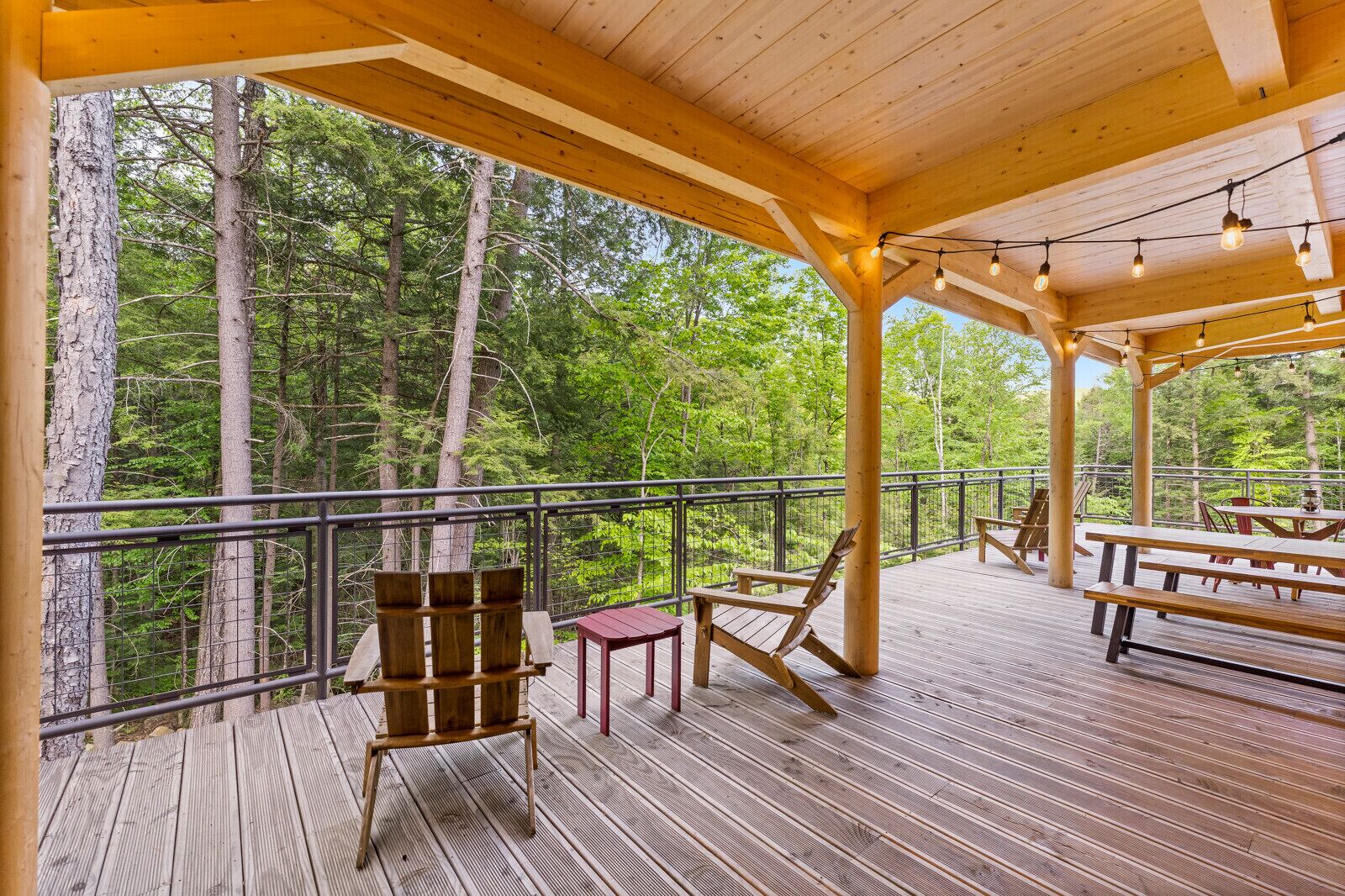 Una terraza de madera con mesas y sillas de picnic, rodeada de un bosque.