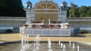 A fountain with multiple water jets in front of a building with a dome and two towers, surrounded by potted plants. - Vacation home Südstrand **** Use of swimming pool, exclusive house with own sauna (Göhren)