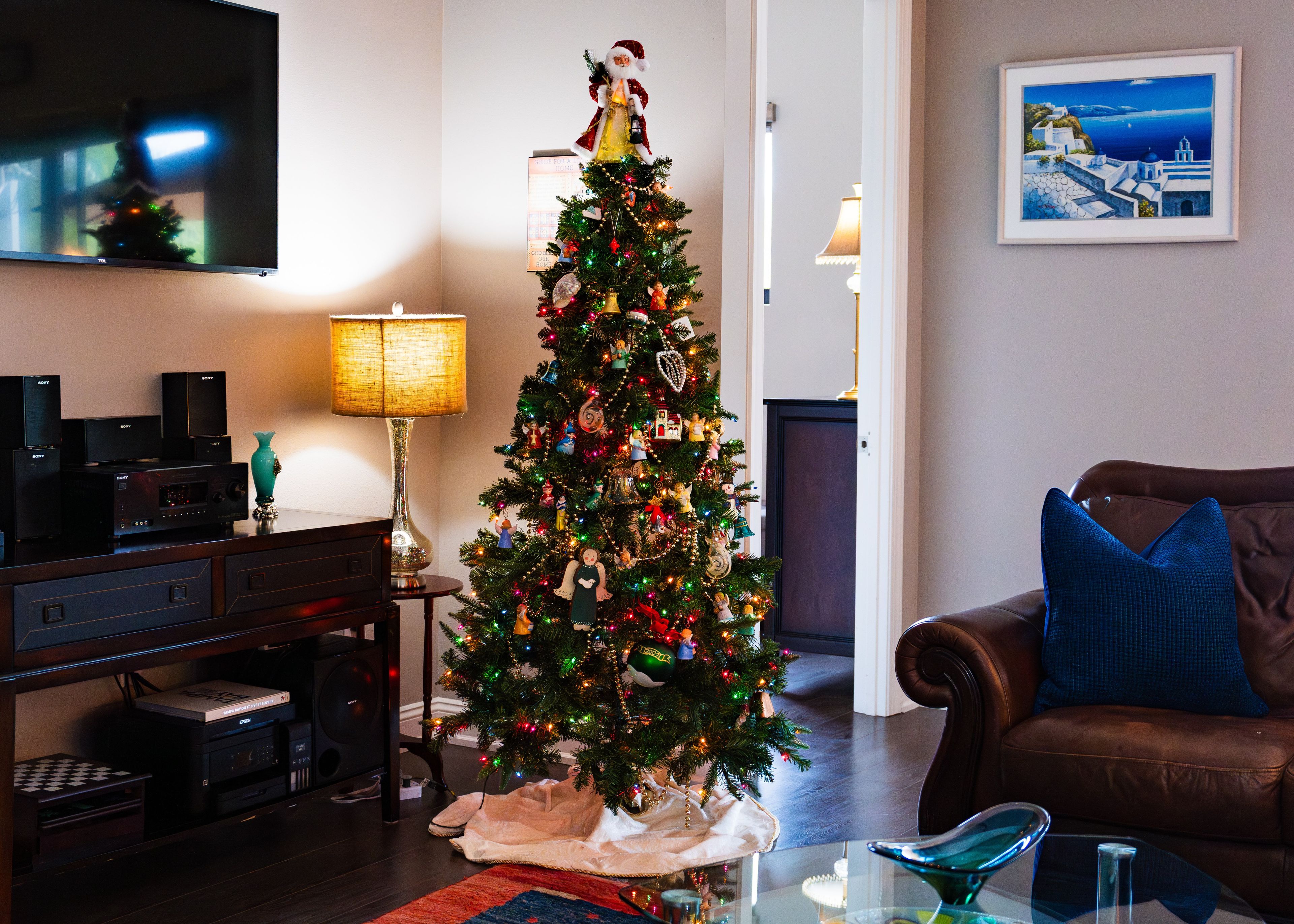 A living room with a Christmas tree, a brown leather sofa, a flat-screen TV, and a framed picture on the wall.