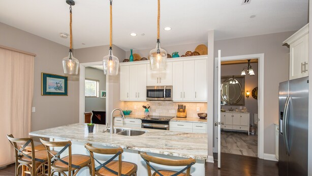 A modern kitchen with white cabinets, a large island with bar stools, stainless steel appliances, and pendant lighting. - Downtown Dunedin Walking District (Dunedin)