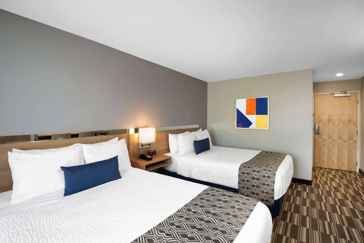 A hotel room with two beds, a wooden headboard, a wall-mounted artwork, and a patterned carpet.