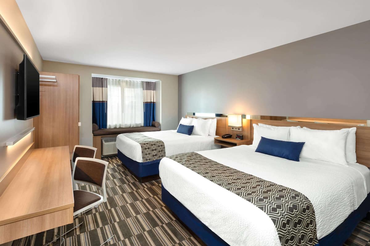 A hotel room with two beds, a desk, a TV, and a window with curtains.