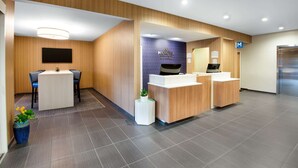 A modern reception area with a wooden reception desk, a seating area with a table and chairs, and a blue wall with the hotel name. - Microtel Inn & Suites by Wyndham Farmington (Farmington)