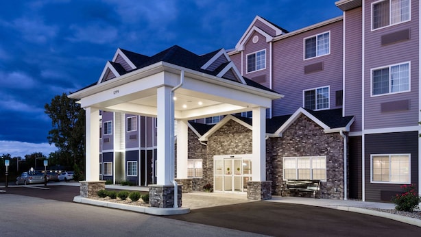 A multi-story hotel with a covered entrance, stone facade, and a parking area. - Microtel Inn & Suites by Wyndham Farmington (Farmington)