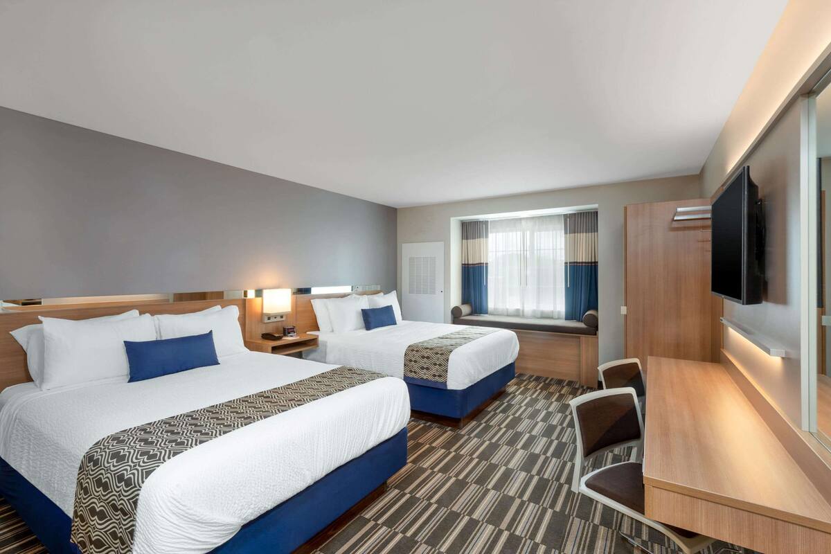 A hotel room with two beds, a desk, a chair, a TV, and a window with curtains.