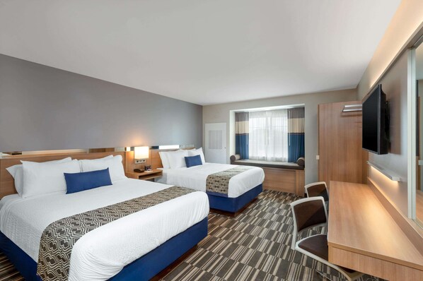 Une chambre d’hôtel avec deux lits, un bureau, une chaise, une télévision et une fenêtre avec des rideaux.