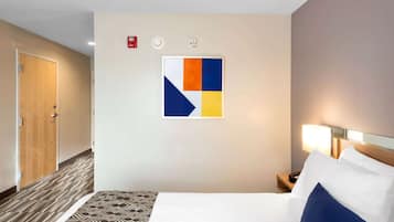 A hotel room with a bed, a nightstand, a wall-mounted artwork, and a patterned carpet.