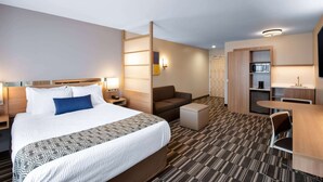 A hotel room with a large bed, a desk, a chair, a sofa, and a kitchenette. - Microtel Inn & Suites by Wyndham Farmington (Farmington)