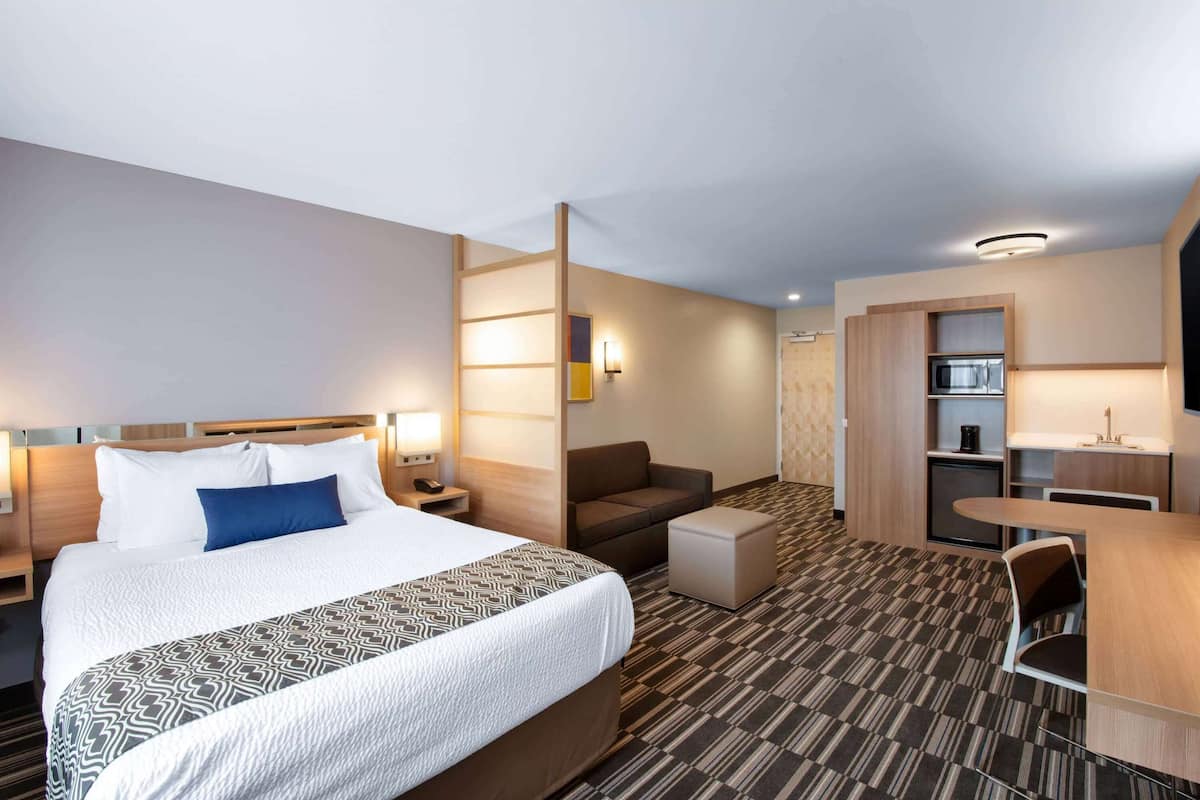 A hotel room with a large bed, a desk, a chair, a sofa, and a kitchenette.