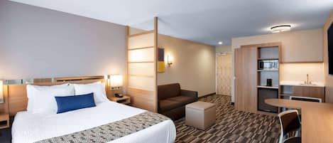 Ein Hotelzimmer mit einem großen Bett, einem Schreibtisch, einem Sessel, einer Sitzecke und einer Küchenzeile.