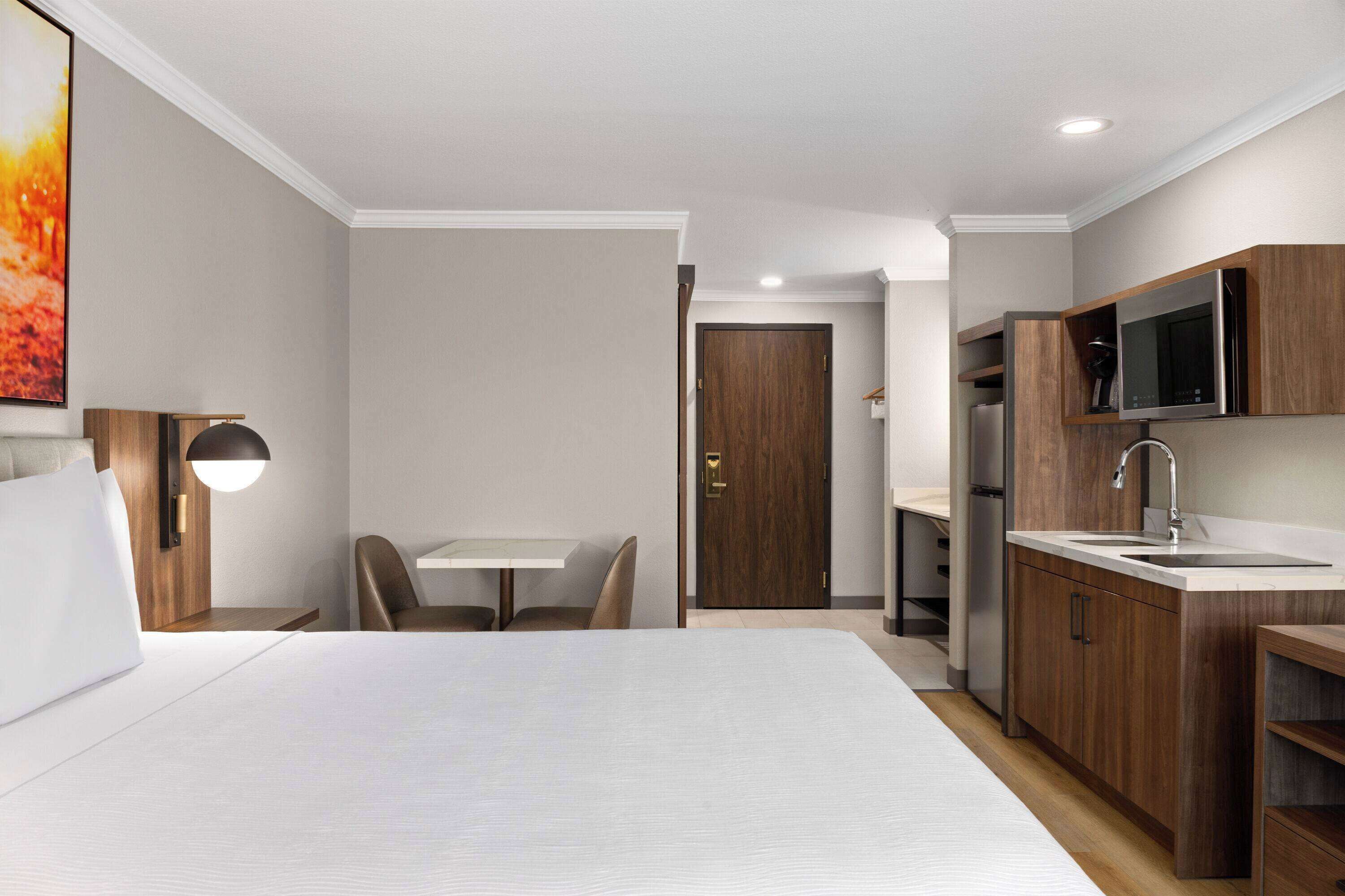 Une chambre d’hôtel moderne dotée d’un grand lit, d’un coin repas, d’une kitchenette et d’une porte donnant sur une autre pièce.