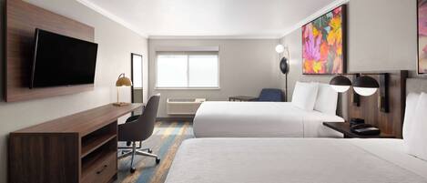Una habitación de hotel con una cama, un escritorio, una silla, un televisor y obras de arte en las paredes.