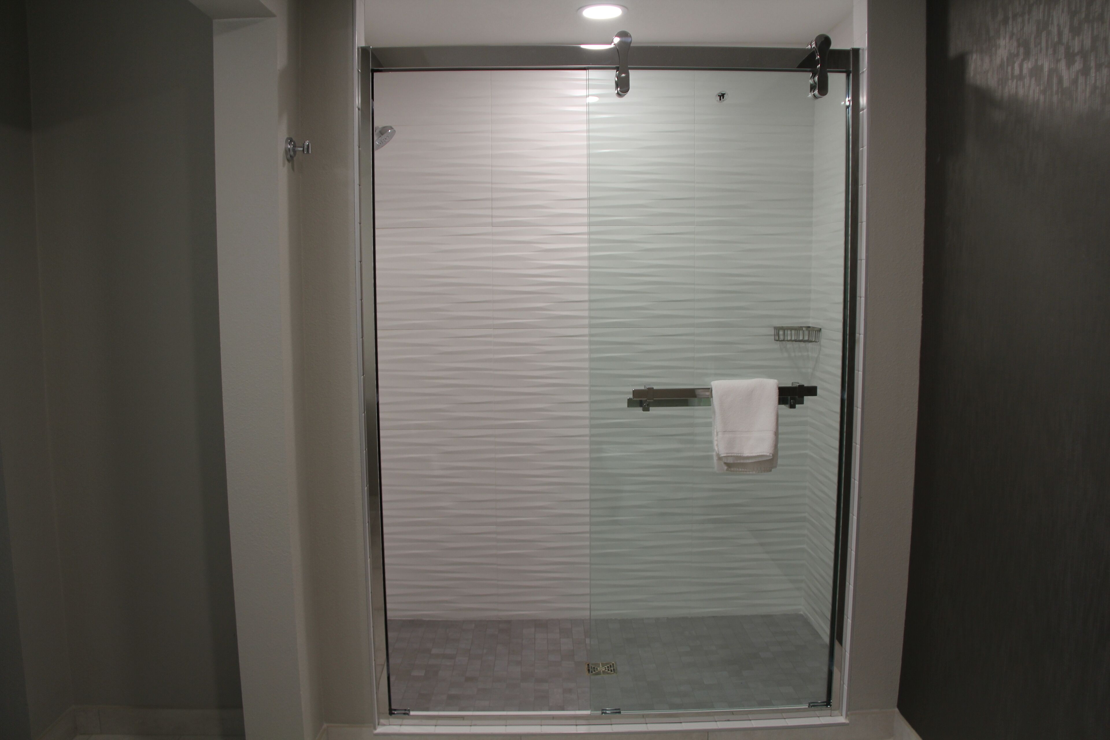 Een douche met glazen wand, een handdoekhouder en een klein plankje.
