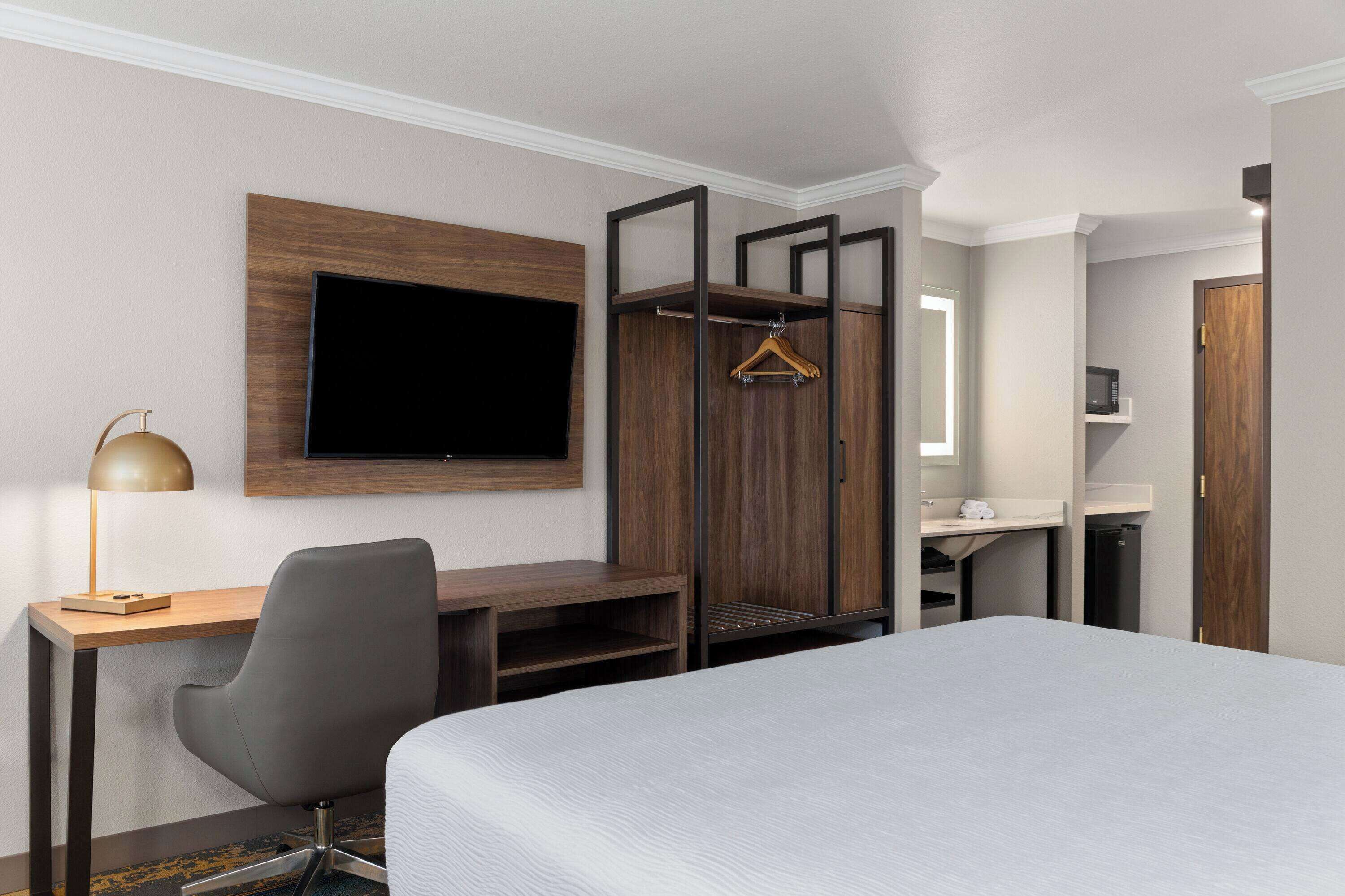 Hotelkamer met een bed, een bureau met stoel, een aan de muur bevestigde televisie, een kledingkast en een klein badkamergedeelte.