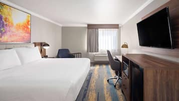 A hotel room with a large bed, a desk, a chair, a flat-screen TV, and a painting on the wall.