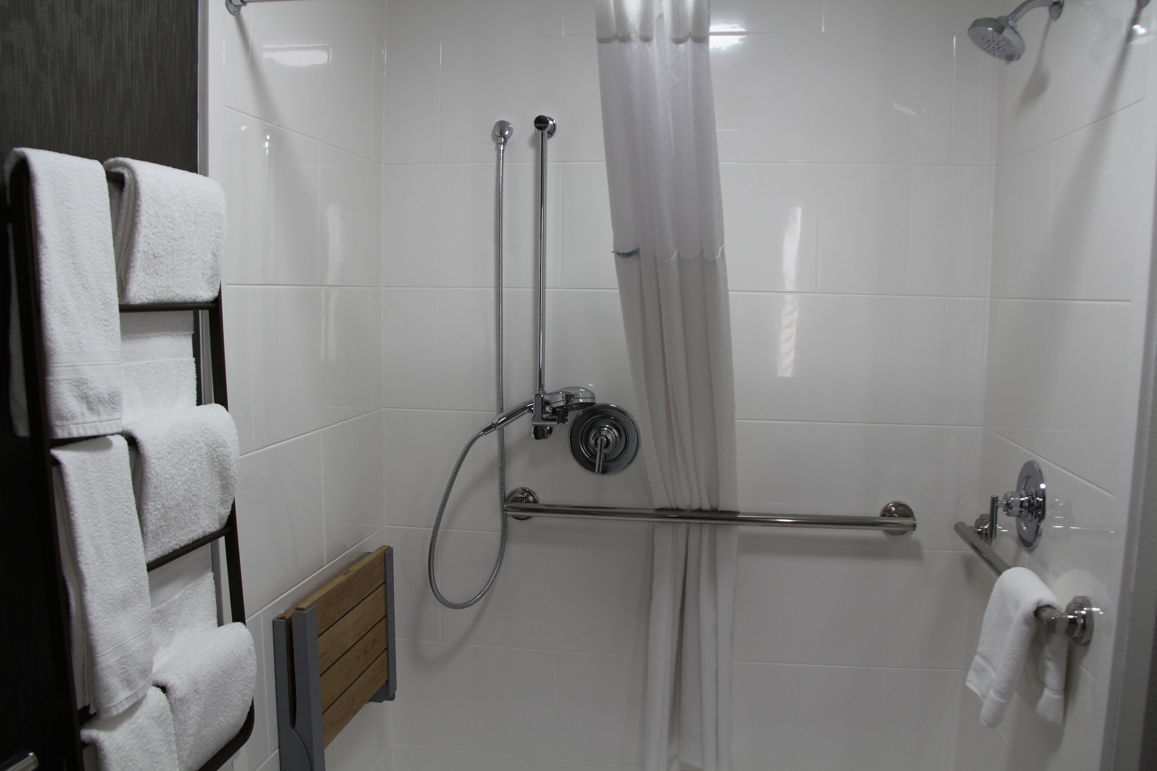 A shower area with a glass door, a towel rack with folded towels, and a handrail.