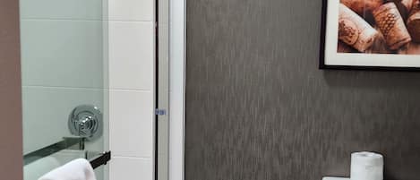 Une salle de bain moderne avec une douche à parois de verre, des toilettes blanches et un tableau encadré représentant des bouchons de bouteilles de vin, accroché au mur.