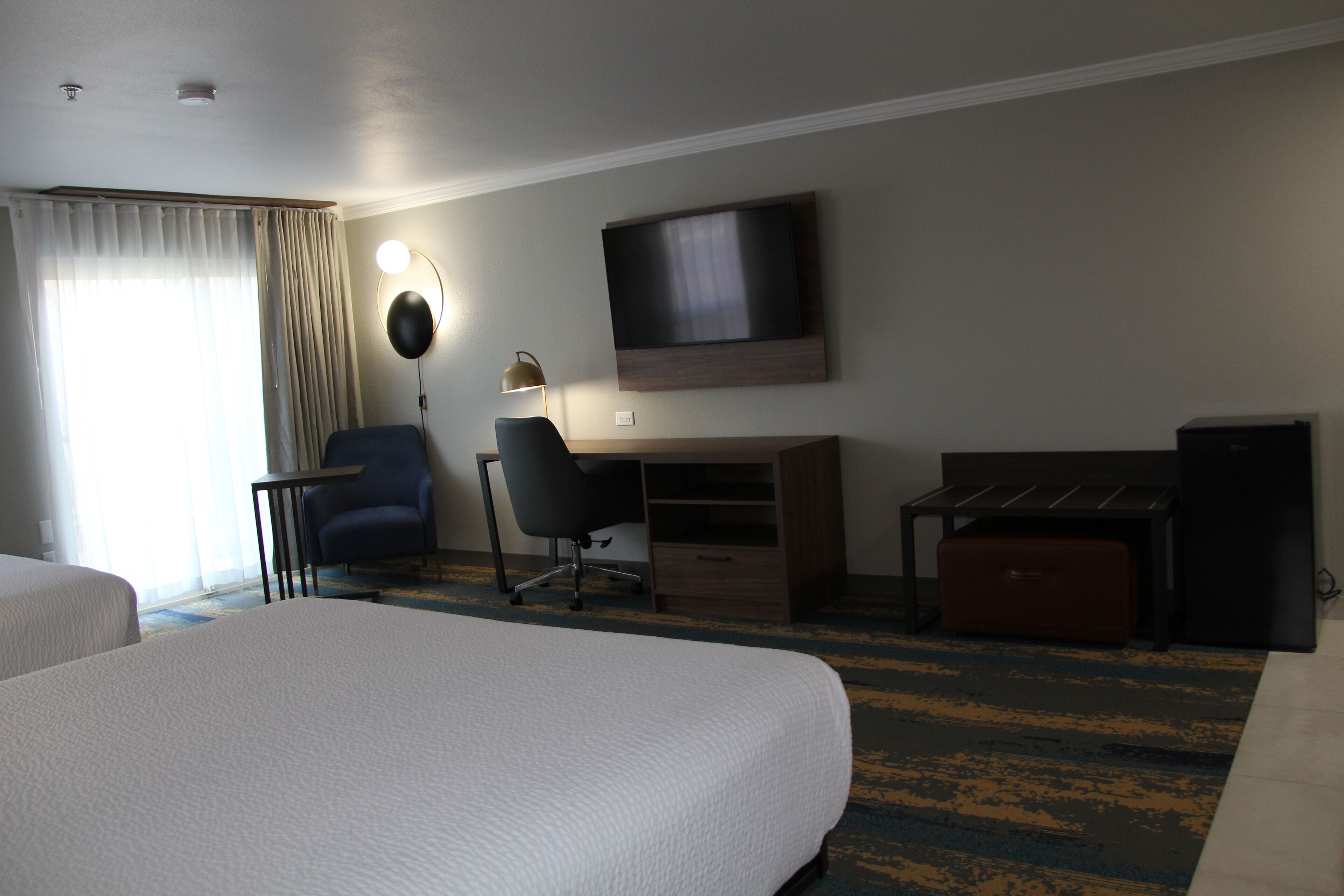 A hotel room with a large bed, a desk with a chair, a television, and a small cabinet.
