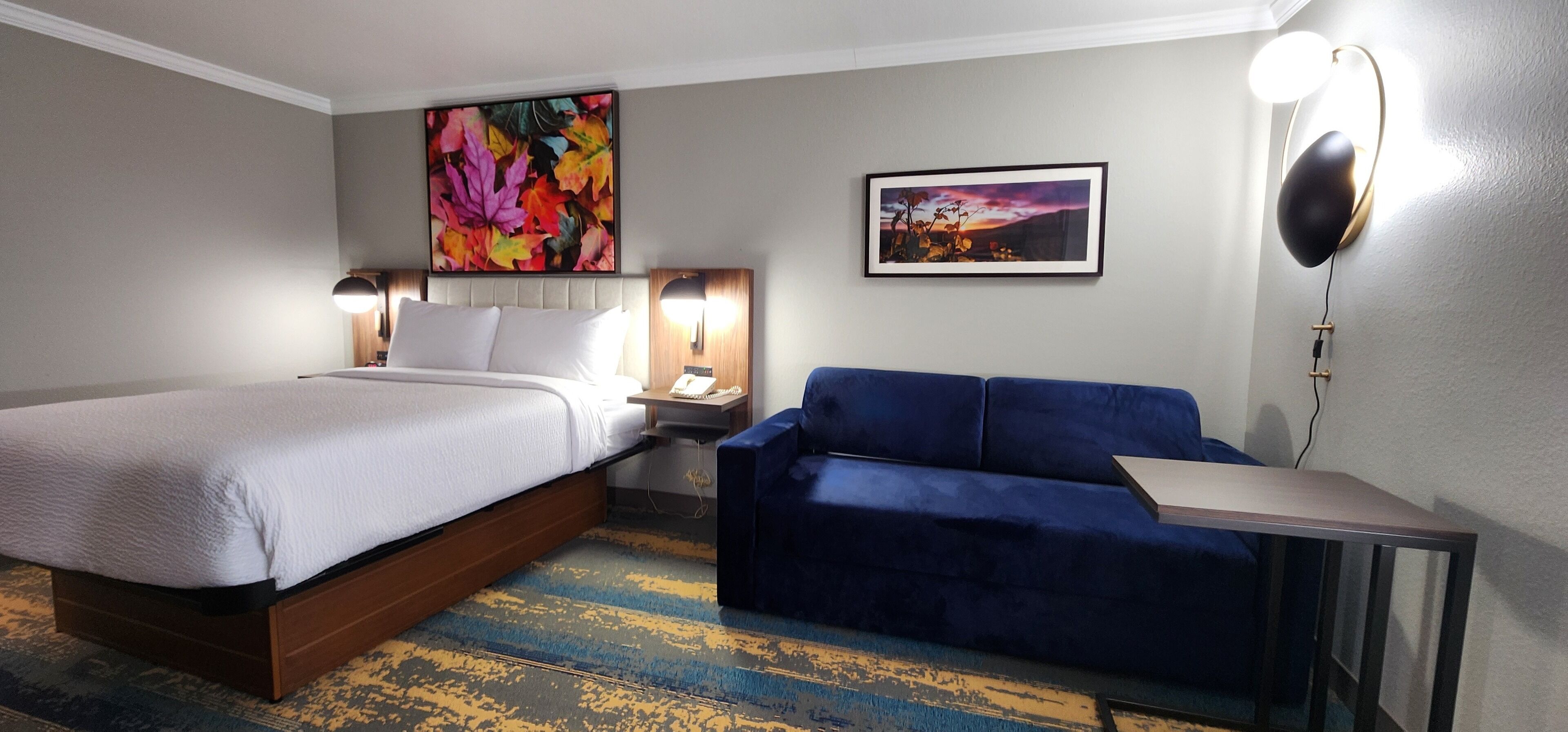 Ein Hotelzimmer mit einem Bett, einem blauen Sofa, einem kleinen Tisch, einem Nachttisch und zwei Wandlampen.