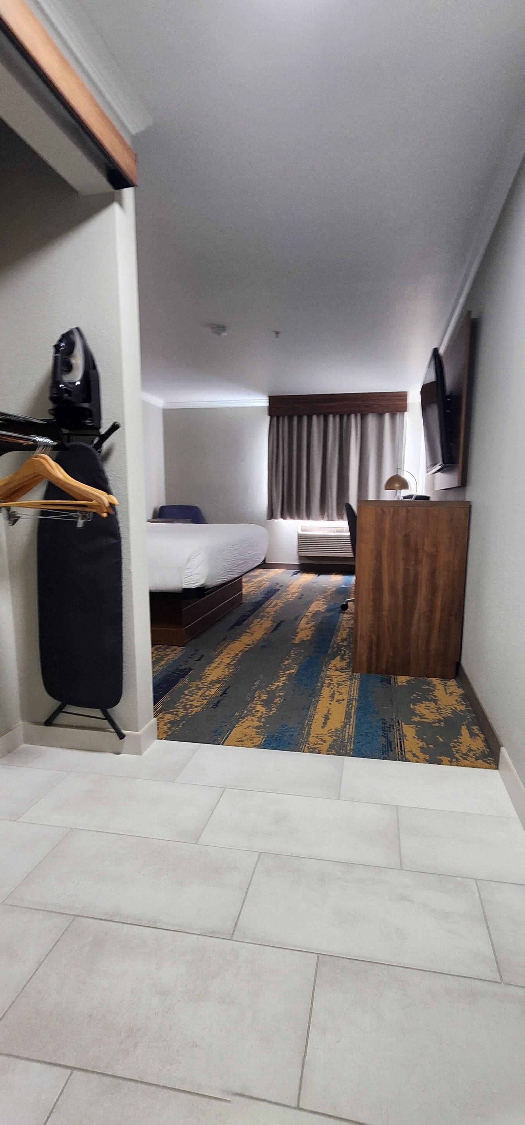 A hotel room with a bed, a desk, a TV, and a patterned carpet.
